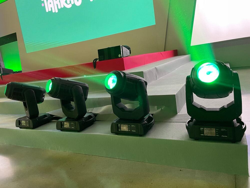 Cabezas móviles con luz verde junto al escenario de un evento corporativo